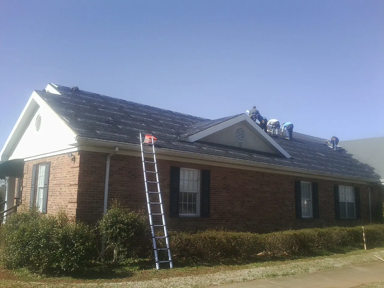 Crew tearing shingles off a brick ranch roof with a ladder set — Metal Roof Repair work by our crew in Nevada City