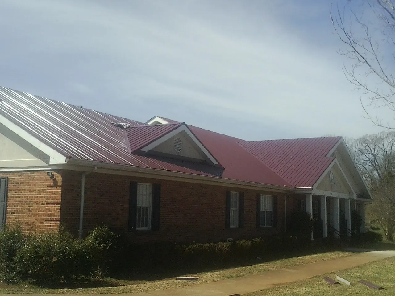 Red metal roof with gabled entries on a long brick building, from a Hail Damage Roof Repair job in Nevada City