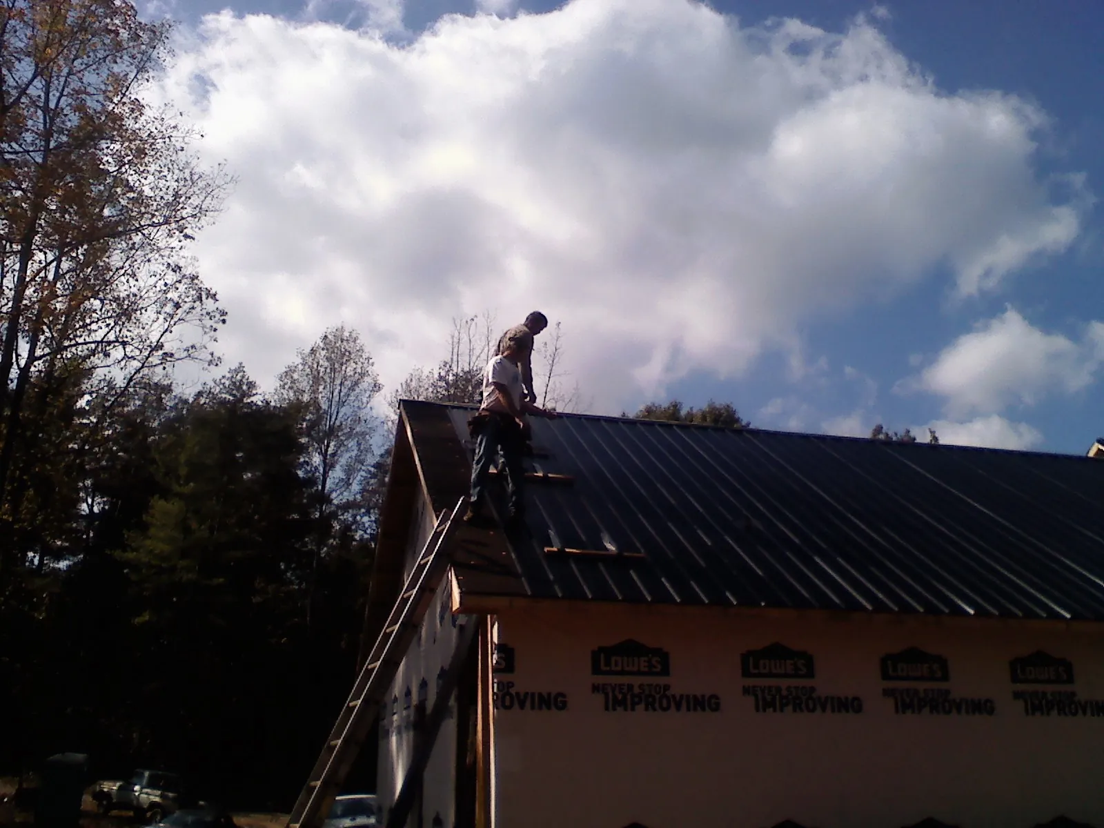 Roofer fastening dark metal panels high against a cloudy sky, from a Roof Inspection job in Nevada City