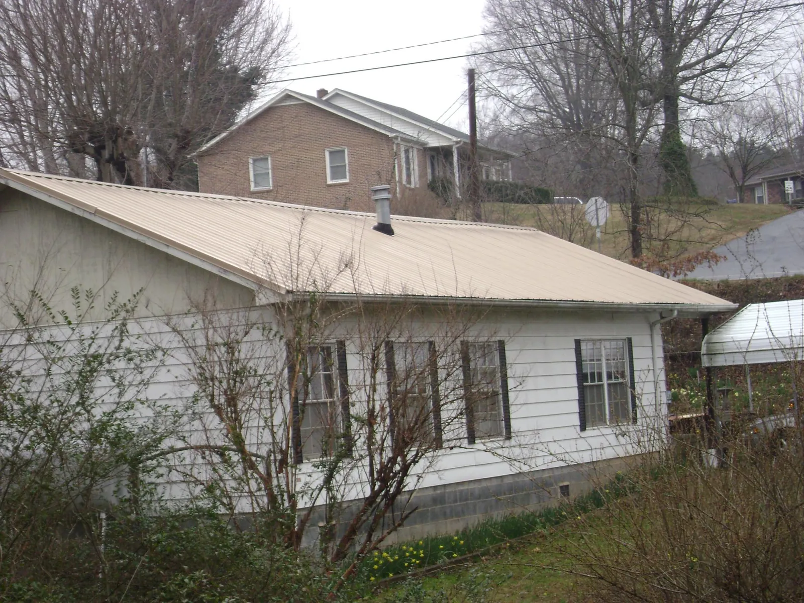 Tan metal roof on a white sided house set into a hillside — Commercial Roofing by Roofing Brothers in Nevada City